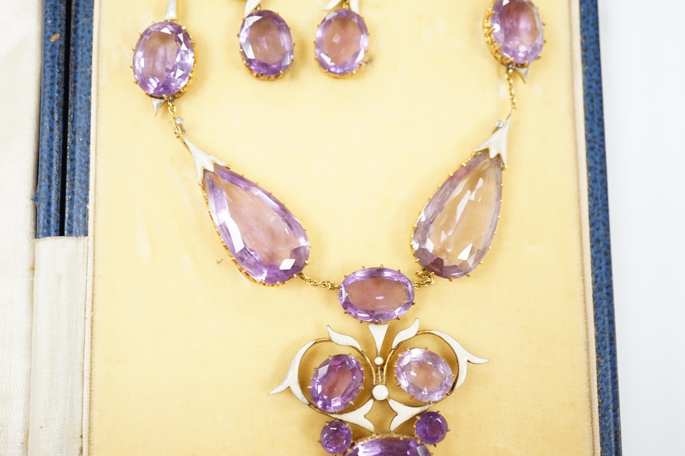 An early 20th century yellow metal, amethyst and enamel set suite of jewellery, comprising a drop necklace, 56cm and a par of matching drop earrings, 33mm, gross weight 38.1 grams.